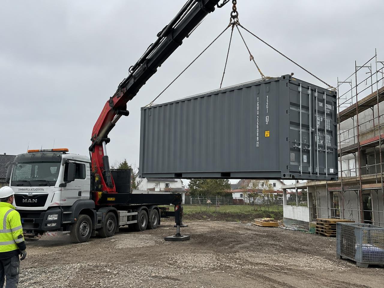 Container wird per LKW-Kran auf einer Baustelle abgesetzt